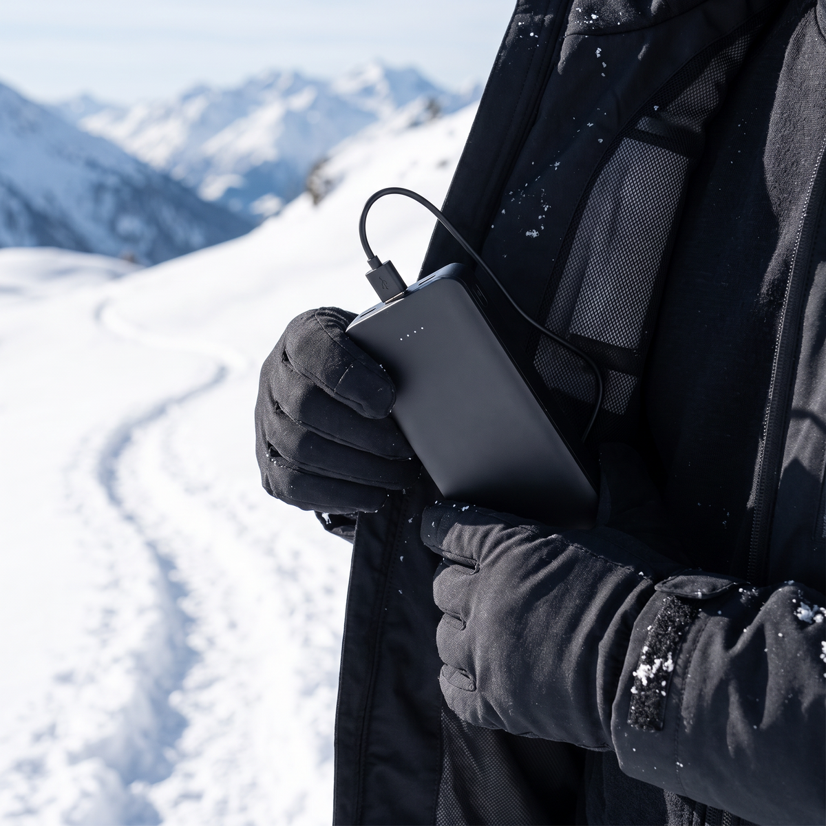 Hiker placing a slim black power bank into a heated jacket pocket