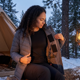 Woman at a winter campsite with black USB heating pads inside her jacket