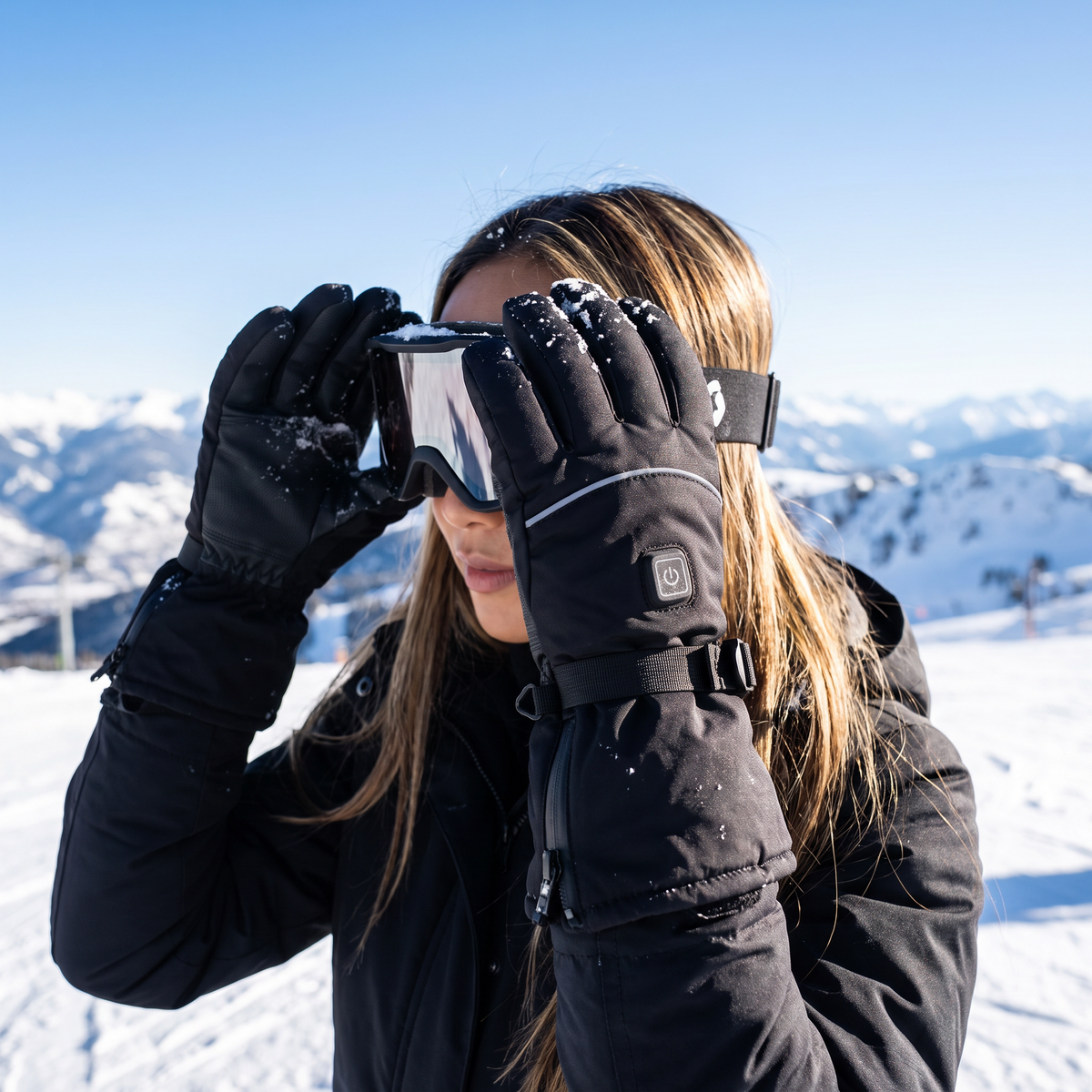 Woman on a ski slope wearing black heated ski gloves