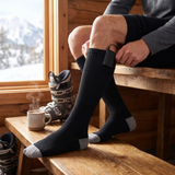 Man in a ski lodge wearing black knee-high heated socks with battery pack